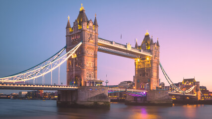 The lights of the iconic Tower Bridge come on at sunset over the Thames in London, England