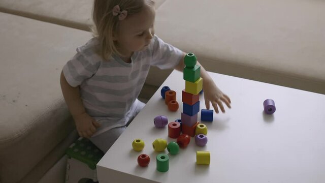 Little girl playing wooden geometrical figures on the table. Sorting rainbow cubes. Hand held Close Up Shot.