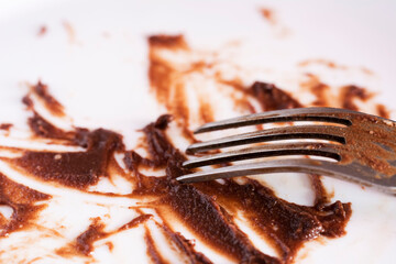 Close up view of dirty fork and white plate eaten chocolate sauce stain. Finished chocolate cake dessert. Concept of enjoy eating.