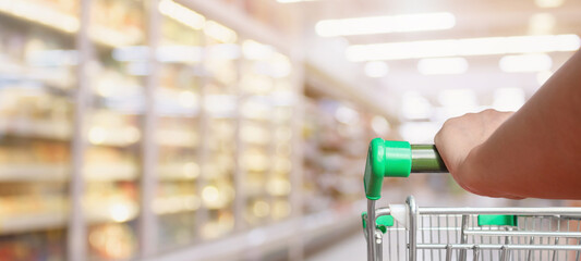 Woman pushing shopping cart with blur supermarket aisle background