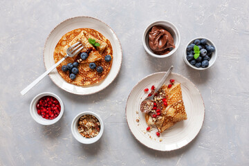Thin pancakes on plate with pomegranate, blueberries, chocolate and walnuts on light background. Top view, close-up
