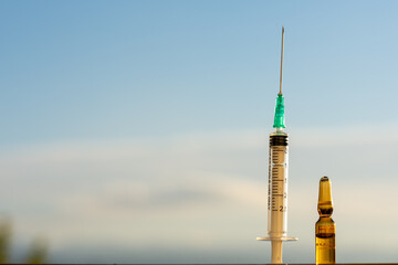 Photograph of a plastic syringe with a needle next to a medicine or vaccine in a glass ampoule with...