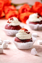 Homemade Red velvet cupcakes with whipped cream, white napkin with ribbon, roses flowers, wooden hearts over pink texture background. Valentines day dessert.