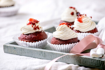 Homemade Red velvet cupcakes with whipped cream on wooden tray, white napkin with ribbon on white linen table cloth.