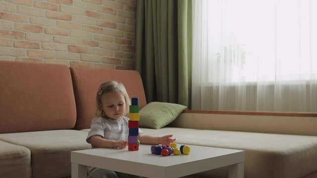 Little girl playing wooden geometrical figures on the table. Sorting rainbow cubes. Medium shot.