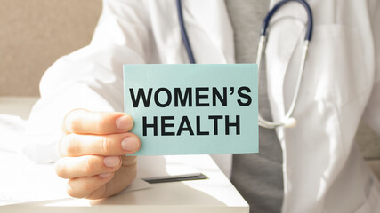 Doctor holding paper with text WOMEN'S CARE, closeup. Health care concept