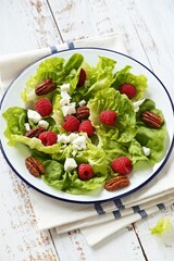 Fresh green salad with raspberry, goat cheese and caramelized pecans on rustic wooden table. Flat layot,copy space