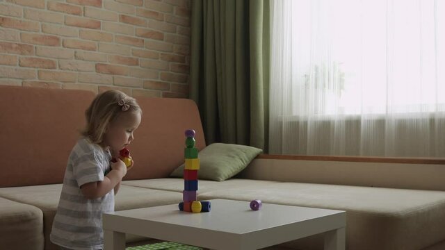 Little girl playing wooden geometrical figures on the table. Sorting rainbow cubes. Medium shot.