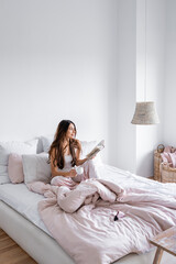 Obraz premium Smiling woman with coffee cup holding book on bed