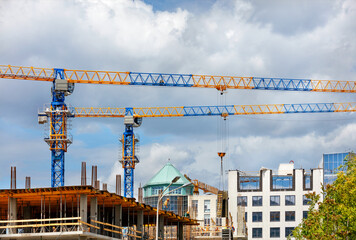 Construction site with tower cranes and the construction of a residential building against the backdrop of a cloudy sky.