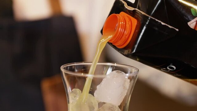 Bartender preparing a cocktail on a bar counter. Pouring orange juice into a crystal glass with ice inside.