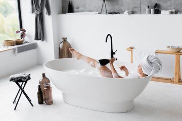 Woman with champagne taking bath in modern bathroom