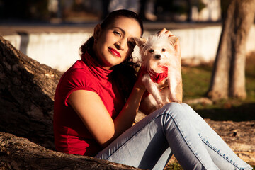 Young girl dressed in red together with her little dog, poured in red, toothed on the trunk of a tree in a natural park.