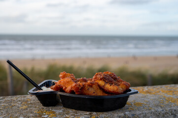 Dutch street seafood, deep fried cod fish fillet with garlic sauce called in Netherlands kibbeling and North sea beach on background