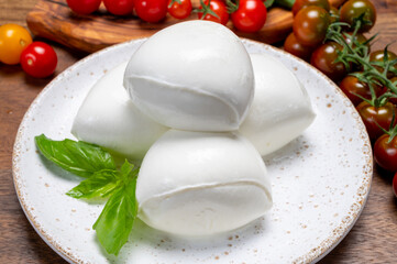 Cheese collection, white balls of soft Italian cheese mozzarella, served with red cherry tomatoes, fresh basil leaves