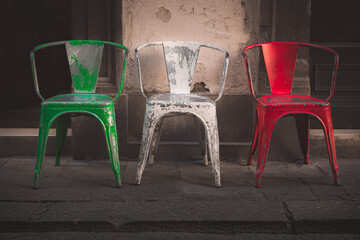 Three chairs line up on the sidewalk to make up the colours of the Italian flag in Florence, Italy.