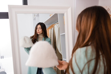 Brunette woman looking at hat on blurred foreground in wardrobe