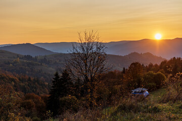 Fantastic sunset in a small mountain village. Panoramic view. Delicate clouds against the orange sky. Colorful autumn in the Ukrainian Carpathians. Beautiful nature scene.