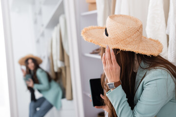 Young woman in sun hat holding smartphone on blurred background in wardrobe
