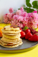 Pancakes with strawberries, pink flowers in the background.