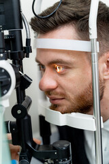 Handsome man is getting an eye exam at ophthalmology clinic. Male is checking retina. Close-up
