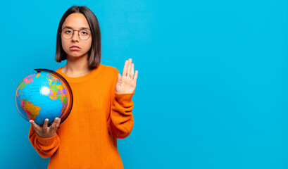 young hispanic woman looking serious, stern, displeased and angry showing open palm making stop...