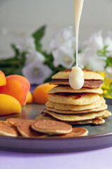Pancakes are poured with white sweet sauce, apricots lie next to them. Selective focus.