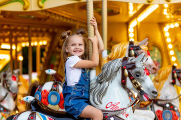 Obraz na płótnie Canvas happy girl in an amusement park rides a horse on a carousel in the summer