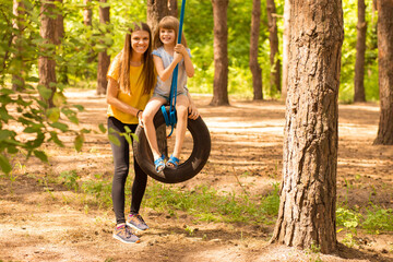 Happy mom and daughter swing on wheel with summer nature background. Active family time together