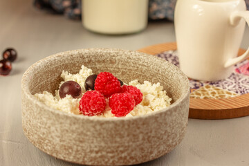 A ceramic bowl of cottage cheese with berries, white creamer on grey background.  Healthy and tasty...