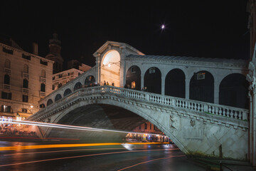 A vaporetto water bus leaves a trail of light at night as under the famous Rialto Bridge in Venice, Italy. - obrazy, fototapety, plakaty