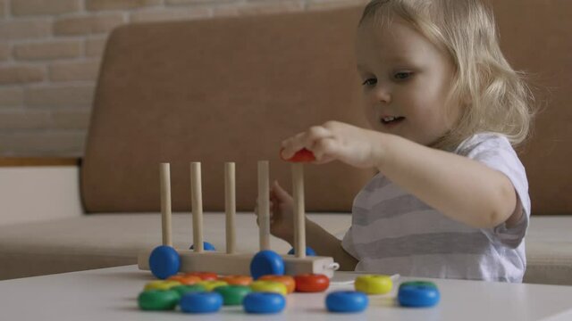 Little girl playing wooden education games on the table. Sorting rainbow wheels. Handheld Close Up Shot.