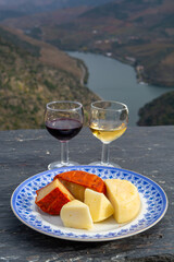 Taste of Portugal, variety of fortified port wines and goat and sheep cheeses, produced in Douro Valley with Douro river and colorful terraced vineyards on background in autumn, Portugal
