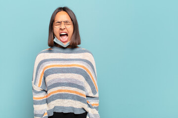 young hispanic woman shouting aggressively, looking very angry, frustrated, outraged or annoyed,...