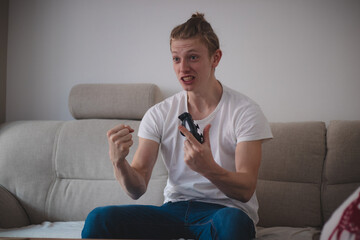 addicted man on a game console sits on a gray sofa, reveling in a successful mission in a strategy...