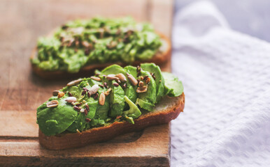 Vegan sandwich with avocado and seeds on a wooden board
