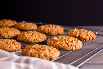 Freshly baked warm oatmeal cookies on a cooling rack on a dark backg