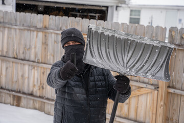 man holding a snow shovel takes a break to give you a thumbs up