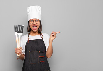 young hispanic woman looking excited and surprised pointing to the side and upwards to copy space
