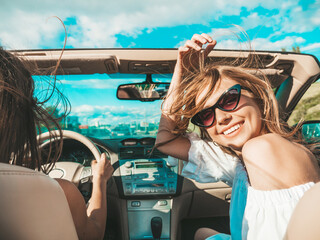 Portrait of two young beautiful and smiling hipster female in convertible car. Sexy carefree women...