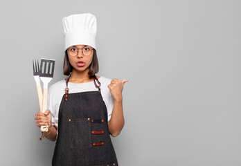 young hispanic woman looking astonished in disbelief, pointing at object on the side and saying...