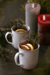 Hot aromatic winter tea with lemon slices and two candles on dark background decorated with christmas tree branches