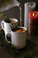 teapot pouring a tea into a teacup with hot tea and slice of lemon on dark background