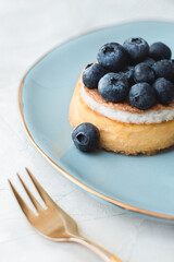 Cheesecake with fresh blueberries on blue luxury plate and a golden fork on light background