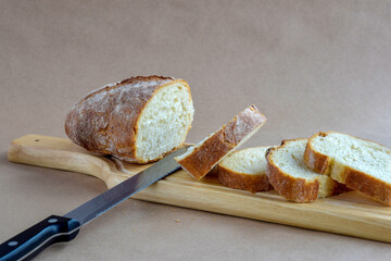 Sliced fresh bread loaf and knife on cutting board. Baked bread lies on table on craft paper, home baked loaf. Natural ingredients. Healthy Diet. Close-up. Selective focus.