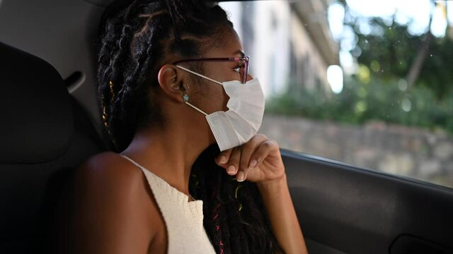 Young black woman in face mask sitting in taxi