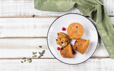 Gluten free muffins with cranberries and pumpkin seeds on a white plate and a mug of vegetable milk on a wooden table. Rustic style. Healthy food
