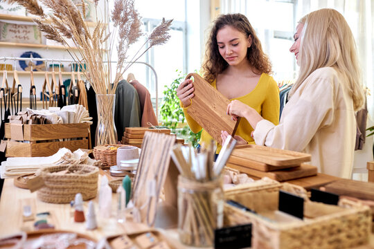 two women buying kitchen items in zero waste shop, looking at them and examining, discussing. eco organic products. minimalist lifestyle concept. shopping at local businesses