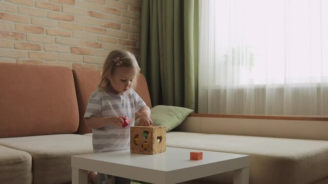 Little girl playing wooden box with geometrical figures on the table. Sorting rainbow cubes. Medium shot.