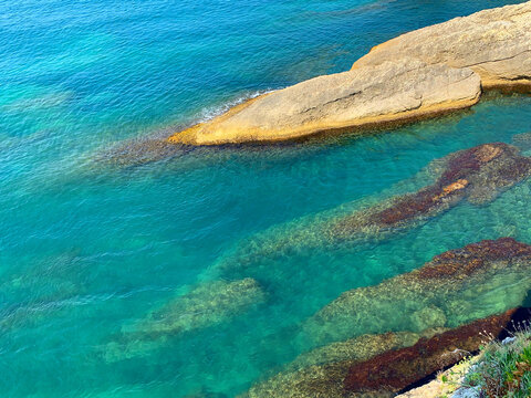 Turquoise sea crystal clear shiny rippled water on rocky paradise island coast beach at summer. Blue ocean waters with seaweed algae. Beautiful lagoon with rocks.